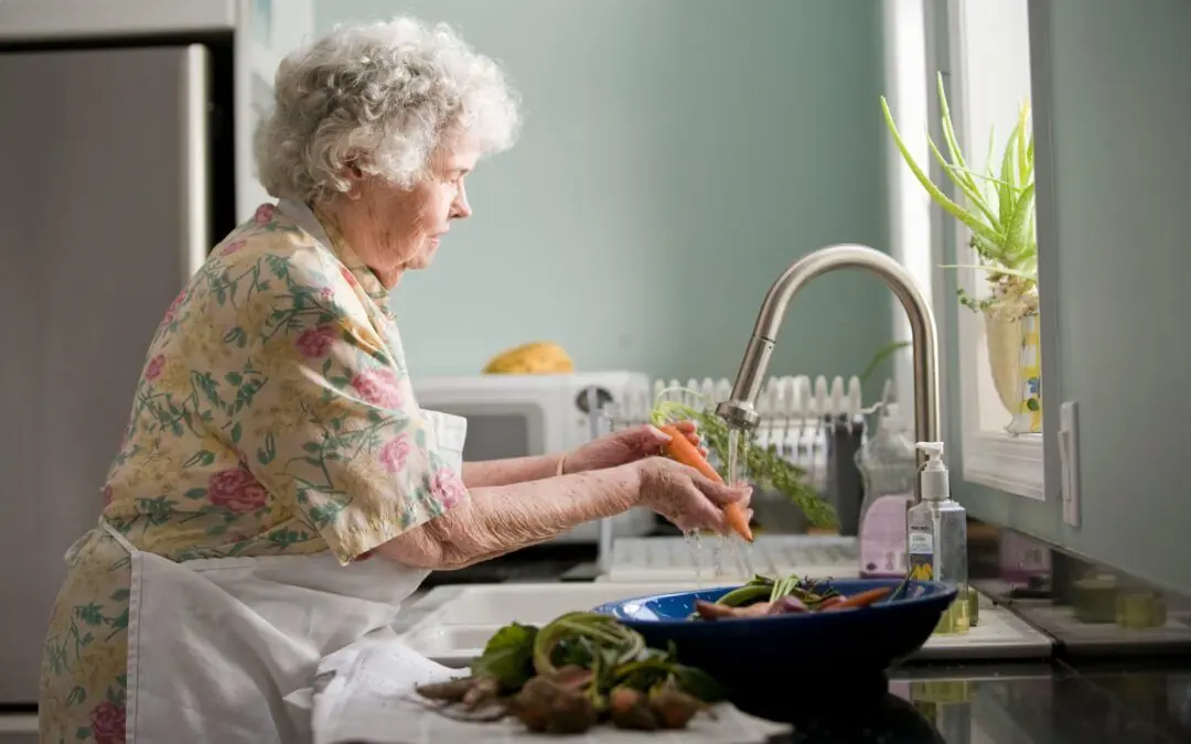 An older woman washing carrots at her kitchen sink.